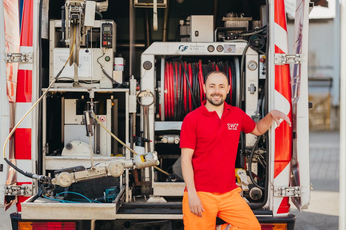 Ein Mitarbeiter der SWO Netz GmbH steht lächelnd vor dem Spülwagen