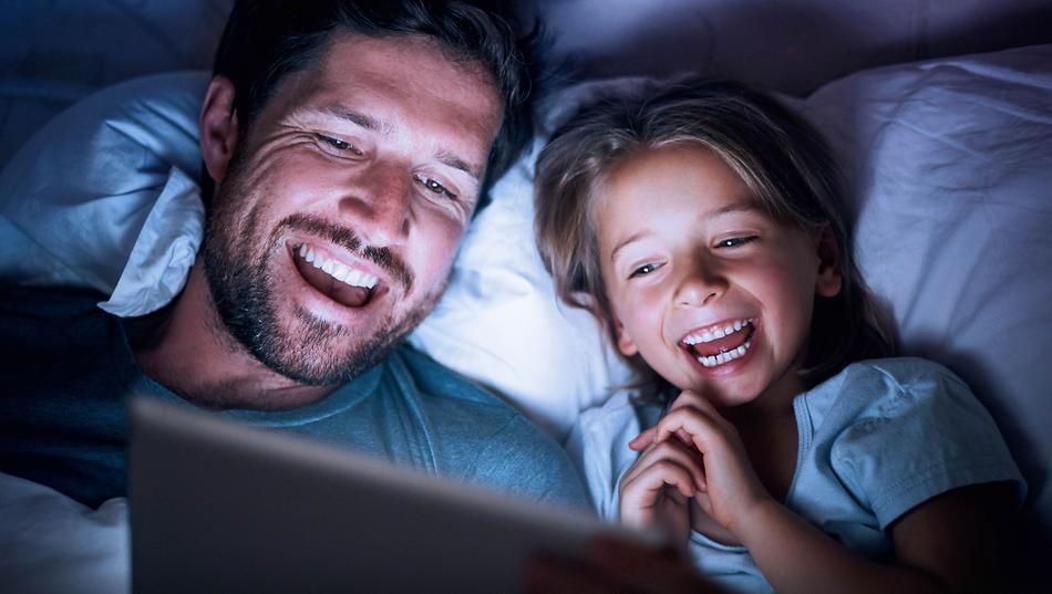 Vater und Tochter schauen im Bett begeistert Waipu TV