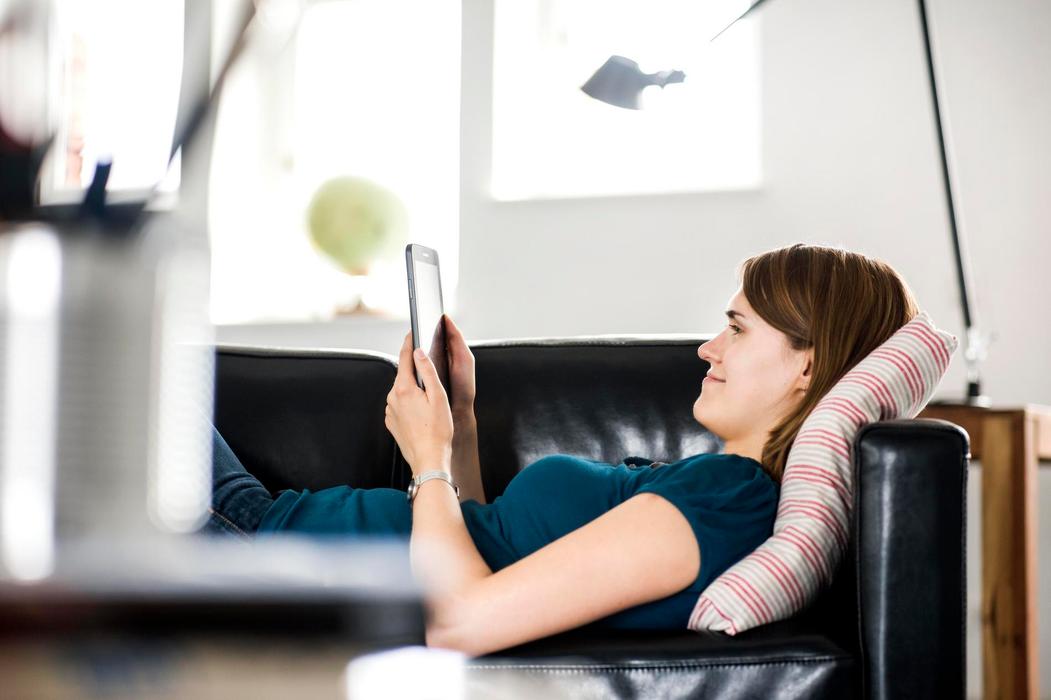 Frau liegt auf dem Sofa und schaut auf ein Tablet