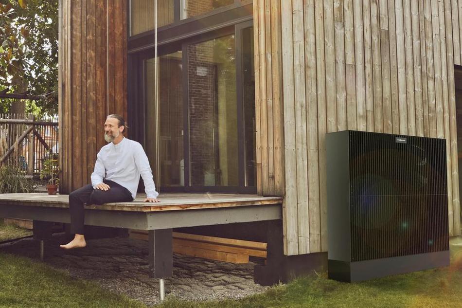 Mann sitzt auf der Terasse eines Hauses mit Wärmepumpe