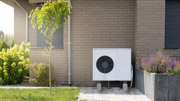 Eine Wärmepumpe steht vor einem Haus. © iStock.com/maxshot