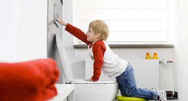 Kind drückt die Spülung der Toilette
