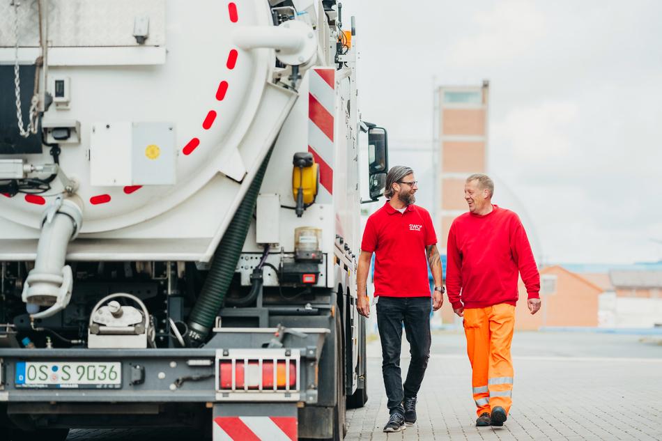 Zwei Mitarbeiter laufen neben dem Spülwagen